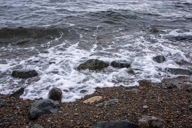 Kıyıdaki büyük taşlar ve küçük çakıl taşları deniz tarafından yıkanır..