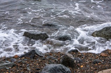 Kıyıdaki büyük taşlar ve küçük çakıl taşları deniz tarafından yıkanır..