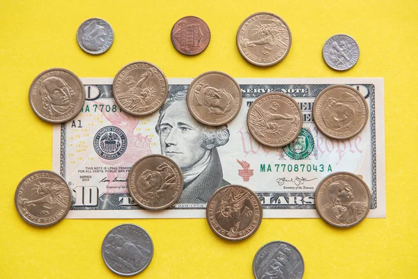 US dollar bills and coins. ten dollar bill and coins of different denominations around on a yellow background.