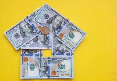 Sarı arkaplanda 100 dolarlık banknotlardan ev şekli.