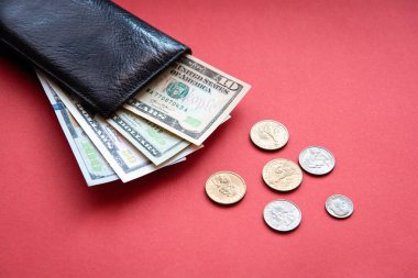 Kırmızı arka planda farklı banknotlar ve madeni paralarla siyah deri cüzdan..
