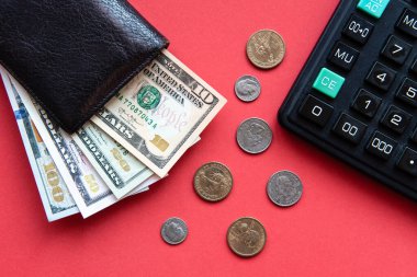 Farklı banknotlar, bozuk paralar ve kırmızı arka planda bir hesap makinesi olan siyah deri cüzdan..