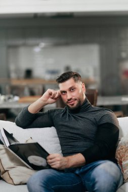 Bir adam elinde kitapla kanepede oturuyor.