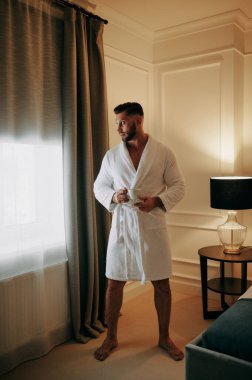 Yatak odasında bir fincan kahveyle bornozlu bir adam.