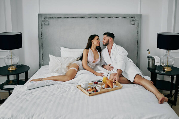 Пара влюбленных в халаты с завтраком в постели