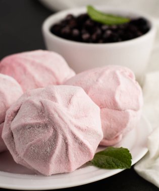 Ön planda pembe şekerlemelerin bulanık görüntüsü ve arka planda bir tabak yaban mersini. Tatlı yiyecek..