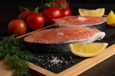 Koyu bir arka planda kırmızı çiğ balık, tuz, limon, dereotu ve domates gibi bulanık besinler. Sağlıklı besinler..