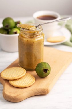 Hafif bir arka planda, bulanık bir feijoa görüntüsü, reçelli bankalar, bir fincan çay ve kurabiye. Doğal tatlı..