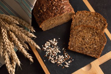 Karanlık bir arka planda, ayçiçeği, keten ve susamlı ekmeğin bulanık bir görüntüsü, bir tahtada parçalara bölünmüş. Sağlıklı yiyecekler. Üst görünüm.