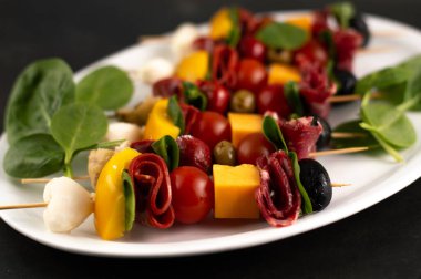 Mozarella, domates, biber, salam, beyaz bir tabakta siyah bir arka planda ıspanak olan aperatiflerin bulanık görüntüsü..