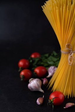 Siyah bir arka planda spagetti, domates, sarımsak ve yeşilliklerin bulanık görüntüsü. İtalyan yemeği..