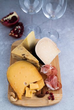 Çeşitli peynir, fındık, jamon, tahta ve nar, şarap bardakları gri bir zeminde. Şarap için..