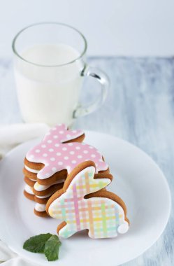 Tabakta tavşan şeklinde çok renkli kurabiyeler, arka planda bir fincan süt. Kalorili gıda..