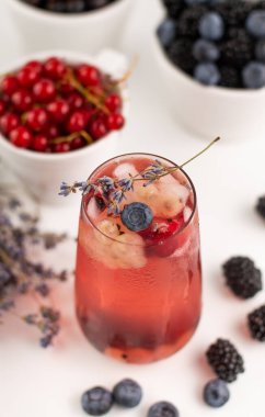 Soğuk bir içecek, böğürtlen, buz ve beyaz bir masada lavantalı bir buket..