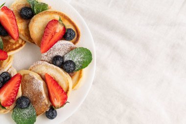 Çilekli krep, yaban mersini, nane şekeri, beyaz bir masada beyaz bir tabakta pudra şekeri..