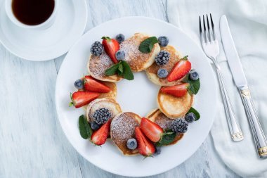 Meyveli krep ve beyaz bir tabakta nane, çatal bıçak takımı, hafif bir masada bir fincan kahve. Lezzetli yemek..