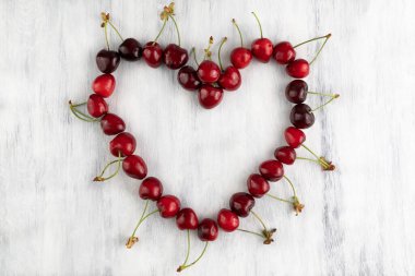 Kalp, gri ahşap arka planda kirazlarla kaplıdır. Meyve arkaplanı.