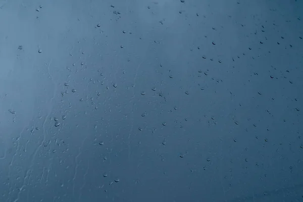 Raindrops on glass against a dark blue sky. Bad weather concept. Texture background.