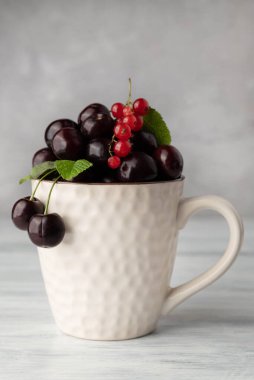 Gri arka planda kirazlı ve kırmızı üzümlü bir fincanın bulanık görüntüsü.
