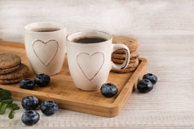 Blurred image of cups with coffee on a tray, cookies and blueberries.