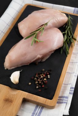 Raw chicken breast, rosemary sprigs, garlic, pepper on a cutting board. The concept of cooking healthy food.
