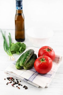 Blurred image of tomato and cucumbers on a towel, basil and onion, olive oil on a light table. The concept of cooking healthy homemade food.