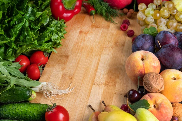 Juicy and ripe vegetables and fruits, berries around a wooden board. Healthy food concept.