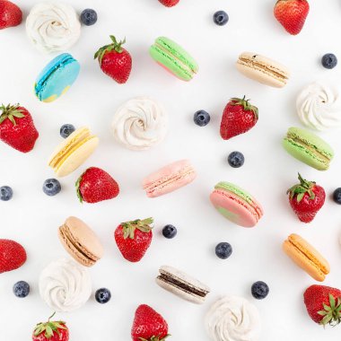 Beyaz arka planda, renkli badem kurabiyeleri, çilekler ve yabanmersinleri.