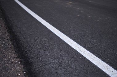 İnşaat halindeki asfalt yolun kenarına beyaz bir çizgi çizilmiş.