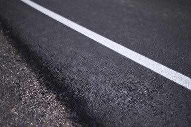 İnşaat halindeki asfalt yolun kenarına beyaz bir çizgi çizilmiş.