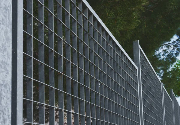 Üzerinde çam ağaçları olan bir yamaçtaki metal çitin ayrıntıları.