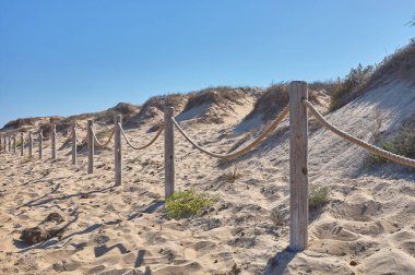 detail of a barrier or railing of ropes and stakes on a beach separating the dunes