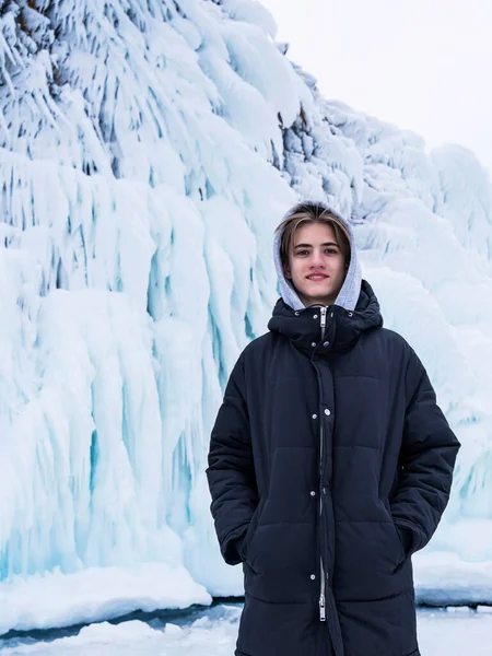 Teenager auf dem Hintergrund einer Eiswand am winterlichen Baikalsee, lässig gekleidet mit Kapuze. Vertikal. — Stockfoto