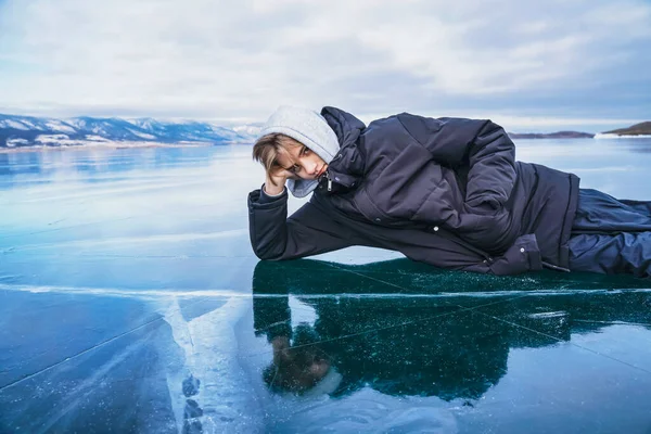 Teenager mit Kapuze liegt auf dem gefrorenen Eis des Baikalsees. — Stockfoto