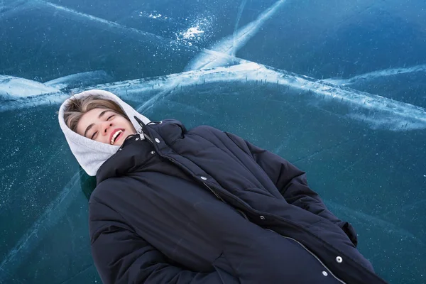 Teenager liegt auf dem Rücken auf dem gefrorenen Eis des Baikalsees. — Stockfoto