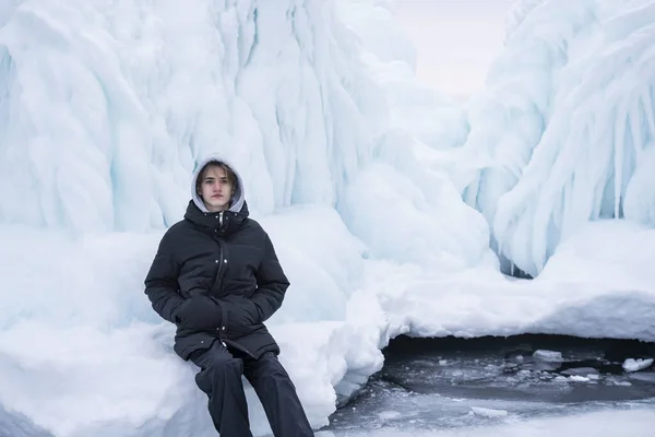 Turista adolescente en una capucha se sienta en el hielo congelado del lago Baikal. —  Fotos de Stock