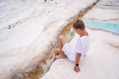 Türkiye 'nin güneybatısındaki travertin havuzlarının önünde oturan genç bir adamın duygusal portresi