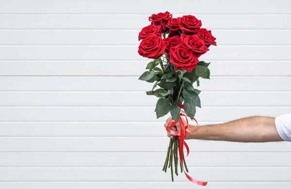 Ramo de flores en la mano sobre un fondo claro. Caballero con un ramo de rosas rojas. — Foto de Stock