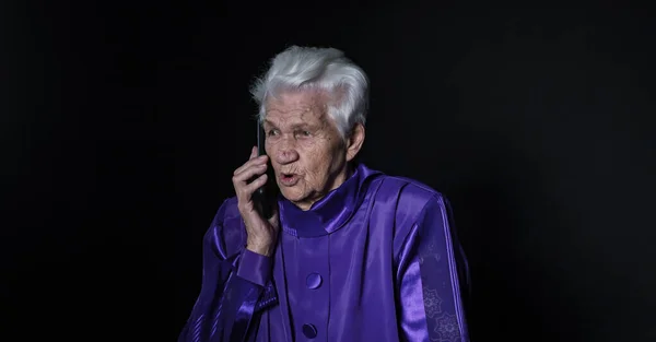Mujer mayor hablando en un teléfono móvil sobre un fondo negro — Foto de Stock