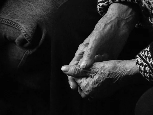 Mãos de uma mulher idosa sobre um fundo preto, o conceito de velhice. Foto em preto e branco. — Fotografia de Stock