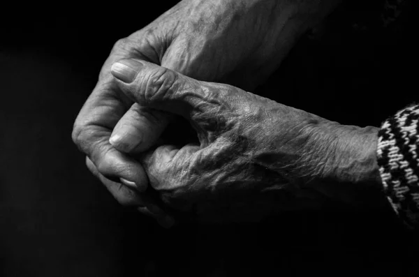 Mãos de uma mulher idosa sobre um fundo preto, o conceito de velhice. Foto em preto e branco. — Fotografia de Stock