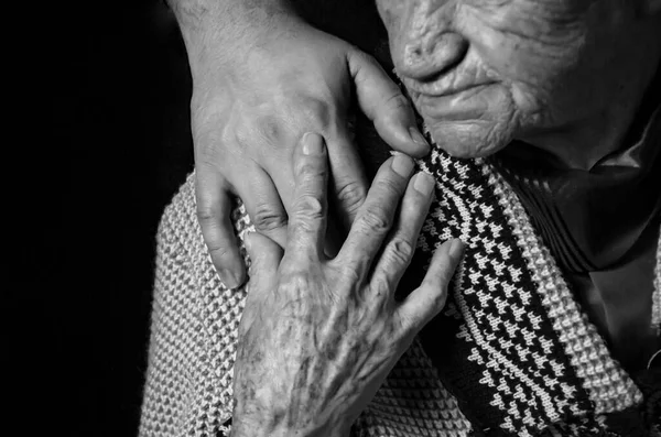 Mãos de uma mulher idosa contra fundo preto. foto preto e branco. — Fotografia de Stock