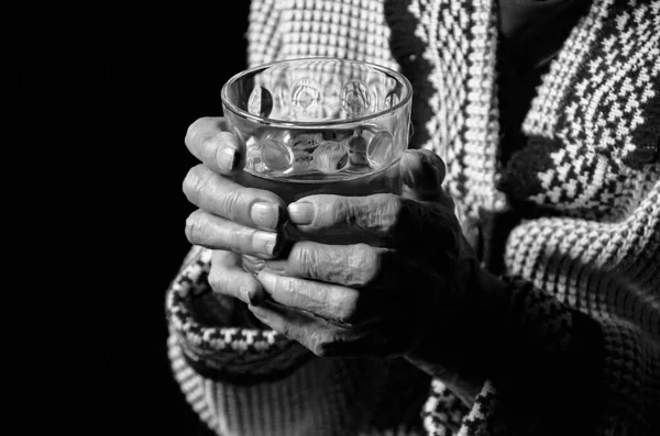 검은 배경에 물 한 컵을 갖고 있는 나이든 여성의 모습. 흑백 사진. — 스톡 사진