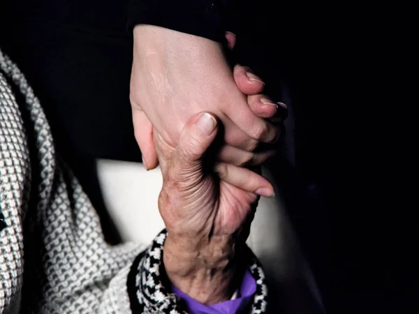 Mãos de uma mulher idosa e uma jovem sobre um fundo preto — Fotografia de Stock