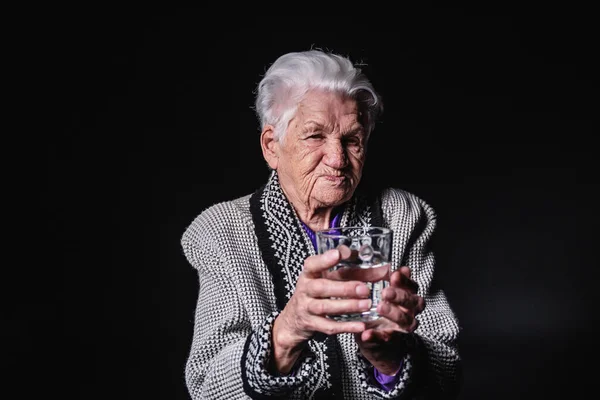 Portret starszej kobiety ze szklanką wody na czarnym tle — Zdjęcie stockowe