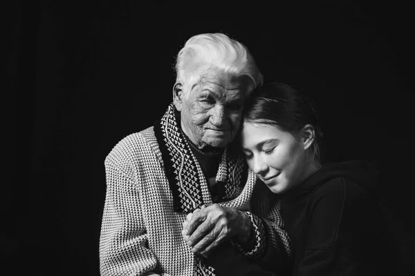 Starsza kobieta siedząca z dorosłą wnuczką w czarnym tle. Czarno-białe zdjęcie. — Zdjęcie stockowe