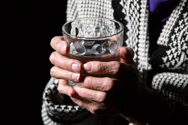 Retrato de uma mulher idosa com um copo de água sobre um fundo preto — Fotografia de Stock