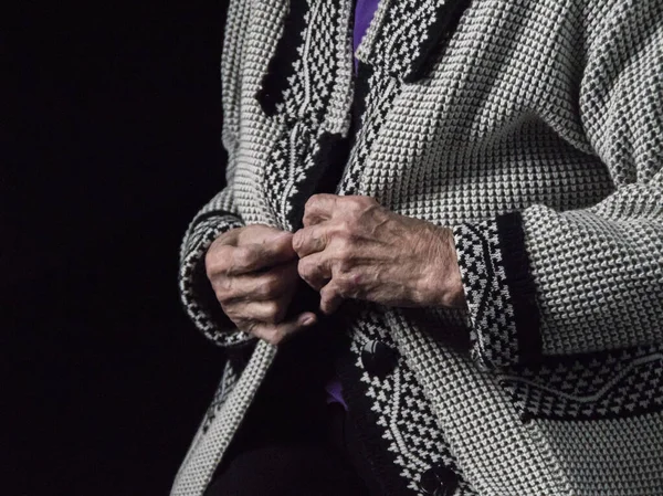 Mãos de uma mulher idosa sobre um fundo preto, o conceito de velhice. — Fotografia de Stock