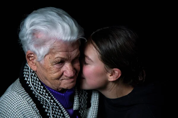 Mujer anciana sentada con una nieta adulta un fondo negro. — Foto de Stock