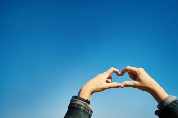 Kız elleri ile zengin mavi gökyüzünün arka planında bir kalp yapıyor.